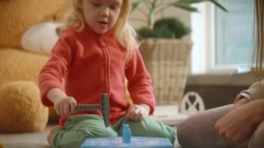 Eğitim oyunları konsepti. Yerde yatan sevimli çocuk annesiyle çekiç ve diğer figürleri kullanarak masa oyunu oynuyor. Gerçek çocukların ilgisi ve duyguları vardı. Heyecanlıydı, eğleniyordu. Yüksek kalite 4k görüntü