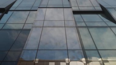Clouds reflected at large glass windows of modern office building, bottom view. Urban landscape, well-maintained office center complex. Architecture details. Slow motion high quality 4k footage