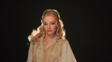 Özel bir ortadoğu elbisesi giyen muhteşem sarışın kız kameraya bakıyor, yavaşça hareket ediyor, kültürel mirası olan Arap zarafeti, zarafet hissi. Zıtlık arka planı. Yüksek kalite 4k görüntü