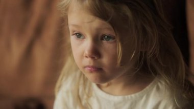 Bir kız çocuğunun portresi, koltukta oturup, evde smth 'i izleyen ciddi bir çocuğun yan görüntüsü. Yüksek kalite 4k görüntü