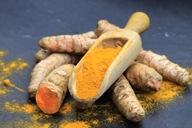 Tahta bir kaşıkta zerdeçal tozu (Kurkuma) ve koyu bir masanın kökleri (curcuma longa))