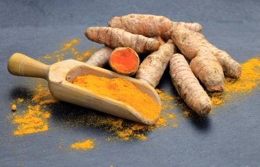 Tahta bir kaşıkta zerdeçal tozu (Kurkuma) ve koyu bir masanın kökleri (curcuma longa))