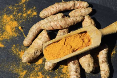 Tahta bir kaşıkta zerdeçal tozu (Kurkuma) ve koyu bir masanın kökleri (curcuma longa))