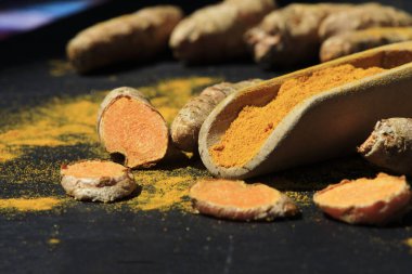 Tahta bir kaşıkta zerdeçal tozu (Kurkuma) ve koyu bir masanın kökleri (curcuma longa))