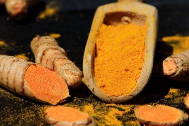 Tahta bir kaşıkta zerdeçal tozu (Kurkuma) ve koyu bir masanın kökleri (curcuma longa))