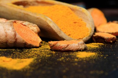 Tahta bir kaşıkta zerdeçal tozu (Kurkuma) ve koyu bir masanın kökleri (curcuma longa))