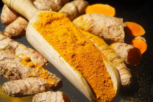 stock image Turmeric powder (Kurkuma) in a wooden spoon and roots 