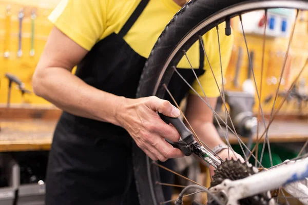 detail of woman\'s hand with pliers fixing bike, unrecognizable girl with black apron and yellow t-shirt adjusting bike parts