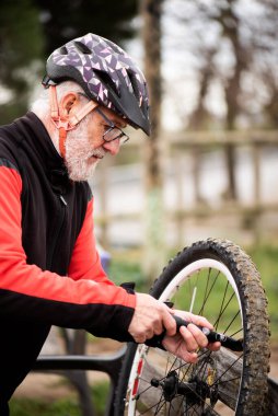 retired older man in cycling clothes, pumping up the wheel of the mountain bike outdoors