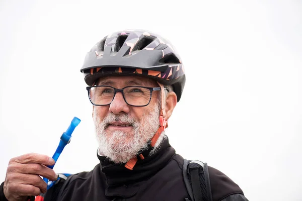 portrait of older male cyclist with beard and gray hair, wearing helmet, drinking pipe water laughing and happy