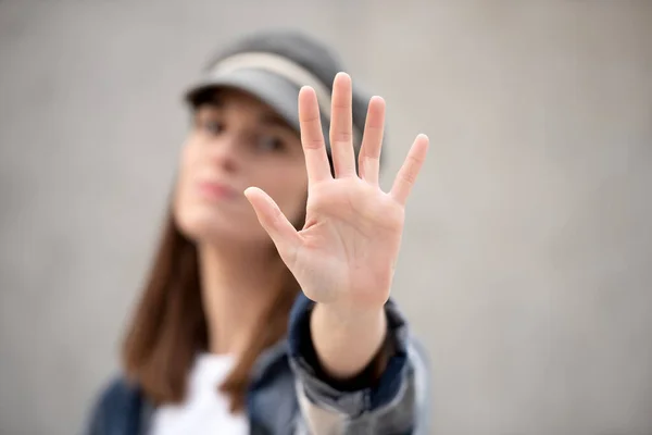 hand saying stop in foreground, in background out of focus girl in cap with serious face