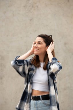 Caucasian girl in jeans and black and white plaid shirt looking to the side with sunglasses on her head, urban gray concrete background