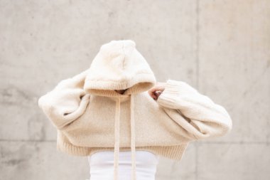 girl wearing a cream sweater with a cap, her face is not visible, monochrome gray-cream shades