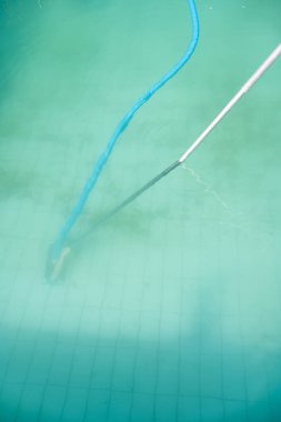 Altında manuel havuz temizleyicisi olan bulutlu havuz suyunun ayrıntıları yüzen bir tüp, mavi renkli su ama berrak değil.