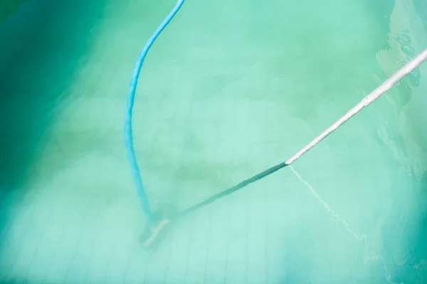 detail of cloudy pool water with manual pool cleaner at the bottom, tube floating, water blue in colour but not clear