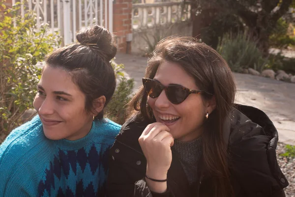 20多岁的孪生姐妹们听着谈话 在户外微笑 一个长头发 戴太阳镜的女孩 一个带着绳结的姐姐 — 图库照片
