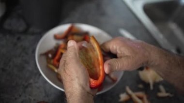 Yaşlı adam büyük kırmızı inek biberi kesiyor, yaşlı adam evde tek başına yemek pişiriyor, seksen yaşındaki baba kızarttığı için biber kesiyor.