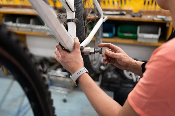 stock image Detail of woman's hand removing nut from bike pedal space, workshop with bike hanging and female mechanic working on maintenance, wrist with smart watch