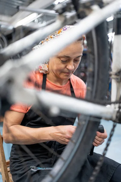 woman working through the spokes of a bicycle wheel hanging in a workshop, mechanic fixing a part and servicing the bike