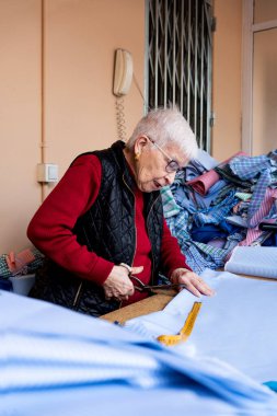 Geleneksel çizgili ve ekoseli büyükannenin elbisesini dikmek için elbise kesen yaşlı bir kadın..