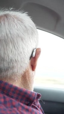 80 'li yaşlarda emekli bir adamın araba kullanırken videosu, şoförden şoföre yardımcı sürücü videosu, gözlüklü ve kulaklıklı ciddi bir adam, yolu izleyen ciddi bir adam.