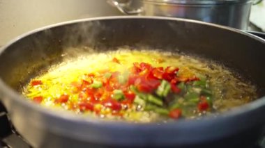 Sofrito, sıcak zeytinyağı yapmak için paella 'ya kırmızı ve yeşil biber atan yaşlı babanın el yapımı videosu. 
