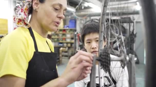 两名妇女参加了多种族社区自行车工作坊 其中一人教另一人如何调整自行车轮 专心致志地检查自行车 — 图库视频影像