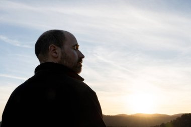 Güneş ışığının son ışınlarına sahip rahat bir adamın portresi. Kırklı yaşlarında, sakallı, kel ve gözlüklü biri..