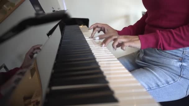 ピアノを弾く白い磁器の爪を持つ女性の手 認識できない女性は楽器の上で練習し フクシアピンクのジャンパーのスツールに座って — ストック動画