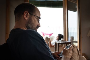 40 'lı yaşlarda bir adam koltukta cep telefonunu izliyor, 20' li yaşlarda bir kadın balkonda odağından kitap okuyor, ailesiyle tatilde dinleniyor..