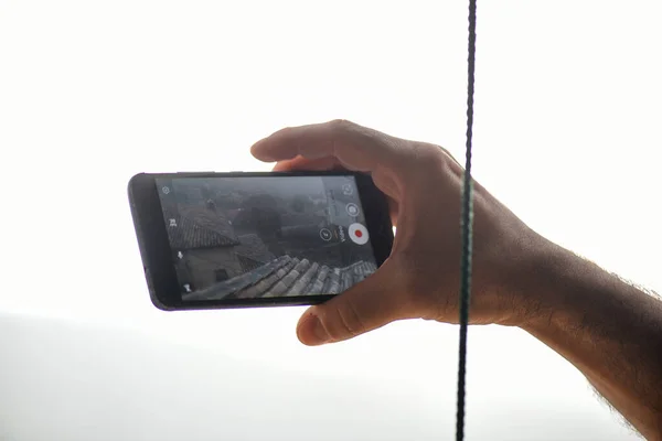 stock image detail of a man's hand making a mobile phone engraving of a rural space with a tiled roof.