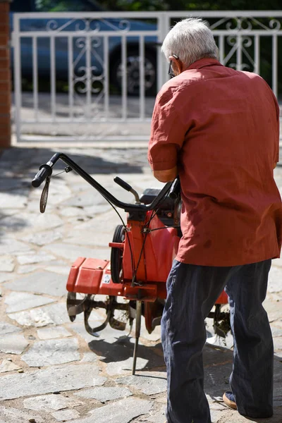 老人背对背 80多岁时还戴着助听器 修理拖拉机 红色农业机械和一件栗色衬衫 — 图库照片