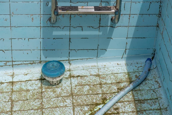 detail of pool robot vacuuming dirt from the floor of an empty and dirty pool with algae, blue and green colours, pool without water due to drought and climate crisis