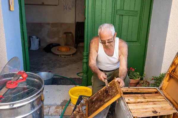 上了年纪的男人为了用离心机提取蜂蜜 把蜂窝门板上的蜡割下来 经验丰富的老人穿着水罐顶盖 — 图库照片