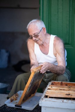 Yaşlı adam bir evin kapısındaki arı panellerini kesiyor. Tank giyen tecrübeli yaşlı bir adam.