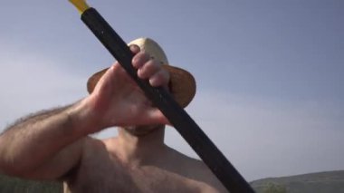 Kırklı yaşlarda hasır şapkalı ve gömleksiz bir adam nehirde şişme bir tekne kullanıyor. Yaz tatilleri ve sıcaklar için dikkat dağıtıcı