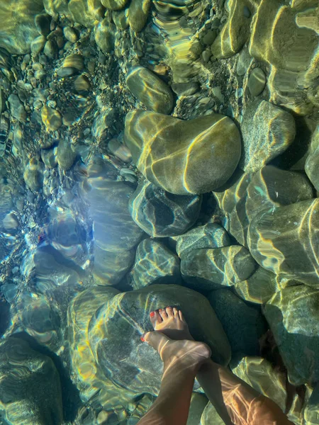 女人的脚在水晶般清澈的河里 有圆圆的石头和倒影 女孩子的脚有粉红的脚趾甲 — 图库照片