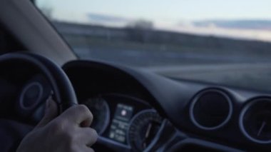 Eller direksiyonda, gün batımı sürüş videosu arabanın içinden geçen yolu görüyoruz. Işıklar açıkken gelen şeritten arabalar geçiyor. Gün ışığının son anları.