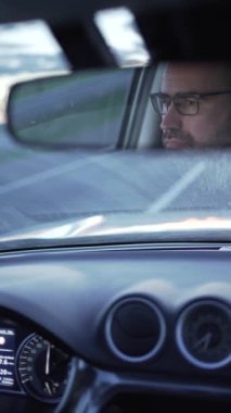 Arabanın dikiz aynasında gözlüklü bir adam. Sürücü yola dikkat ediyor, ön camda ilerleyen yolu görüyoruz, sürüş ve seyahat videosu..