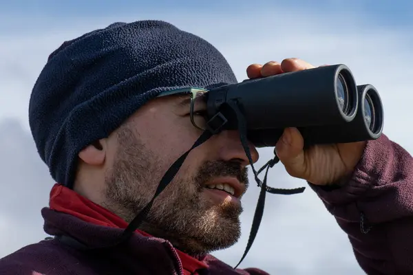 四十多岁的男人穿着山服 戴着眼镜 蓄着胡子 通过双筒望远镜眺望风景 图库图片