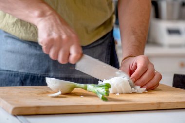 Tahtada soğan doğrayan insan elleri, yeşil tişört, önlük, kot etek.