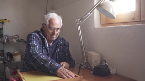 年长的男性养蜂人为蜂箱准备蜡框架 穿着温暖的蓝色格子衬衫 站在有自然光的车间里 — 图库视频影像