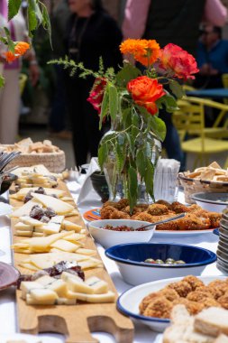 Köy festivalinde popüler bir aperatif için yiyeceklerle dolu kare masa. Patates omleti, peynirler, sosisler, tahta tahtalar ve tabaklar üzerinde kroketler, doğal güllerle dolu vazolar..