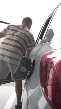 Plastik eldivenli bir adam açık mavi bir arabaya benzin döktü.