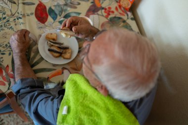 80 yaşında bir adamın kahvaltısını yaparken, sardalyalarla tost yerken ve bir fincan süt içerken zenital görüntüsü..