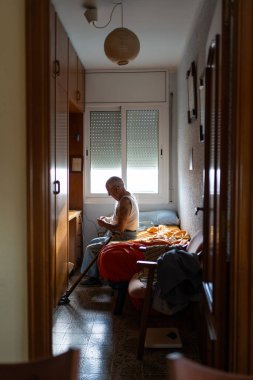 Yaşlı bir adam tek bir odada yatağında oturuyor, sabahları bardaklarını temizliyor..