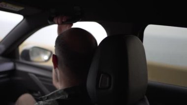 Araba kullanmaktan korkan yardımcı sürücünün yatay videosu, arabanın gidonuna tutunuyor. Kırklı yaşlarda, gözlüklü ve kel kafalı bir adam..