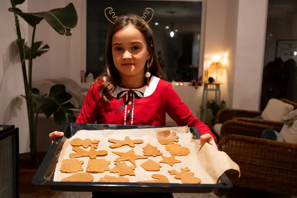 Noel bisküvisi pişirme tepsisiyle kırmızı giyinmiş ve boynunda geyik başlığı olan bir kızın portresi..