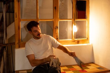 Genç adam elinde iş eldivenleriyle konuşuyor, sıcak ve modern bir evde kırsal bir görünüme sahip.