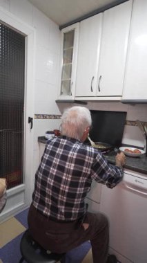 Yaşlı adam tek başına yemek pişiriyor. Yaşlı adam 80 'li yaşlarda, gömlekli.